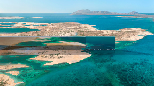 A building resembling a sharp reflective piece of metal cuts through a desert landscape.