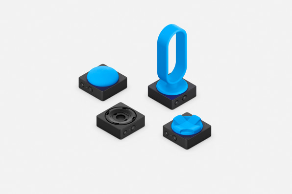 A photo of 3d printed attachments for Adaptive accessories, they are blue plastic and range from large buttons smooth buttons, to directional wedges, to a tall oval loop. 