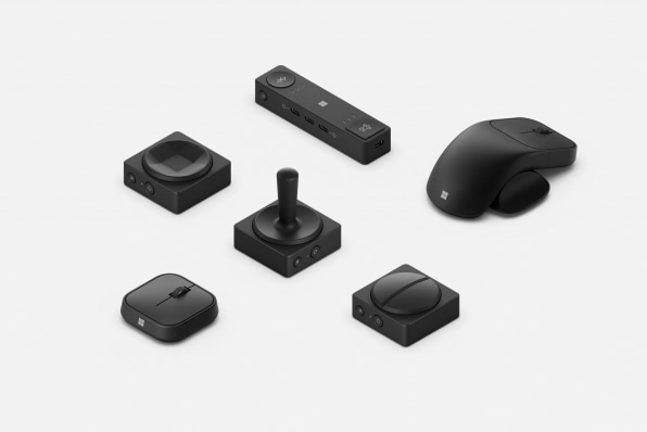 A photographic overview of several Adaptive accessories, they are black plastic objects resembling mice, joysticks, and jumbo-size directional pads similar to those found on video game controllers